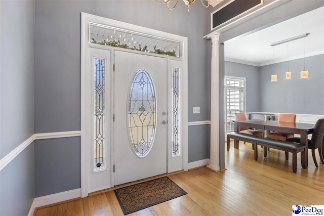 entryway with crown molding, baseboards, light wood-style floors, and ornate columns