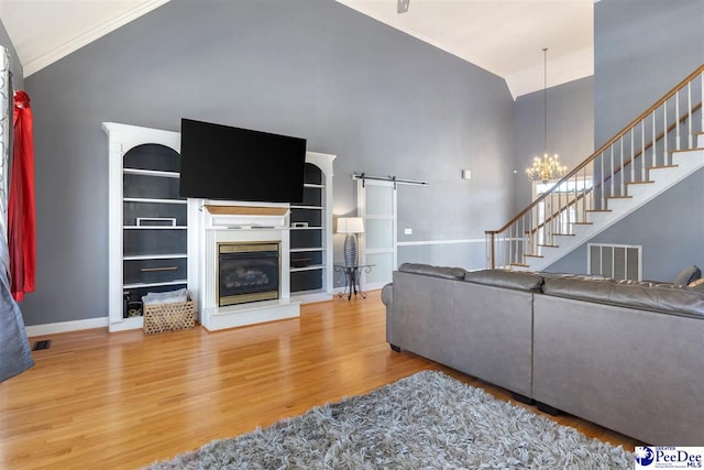 living room with a chandelier, stairs, a barn door, wood finished floors, and high vaulted ceiling