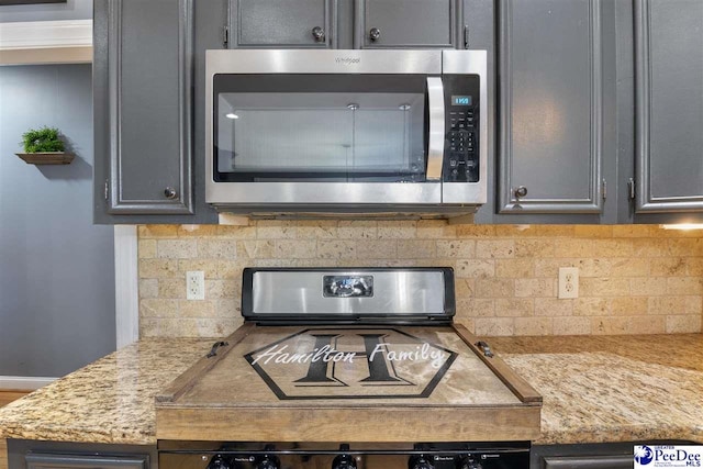 details featuring tasteful backsplash, stainless steel microwave, and gray cabinets