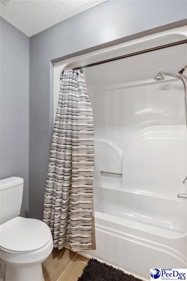 bathroom featuring toilet, wood finished floors, shower / tub combo with curtain, and a textured ceiling