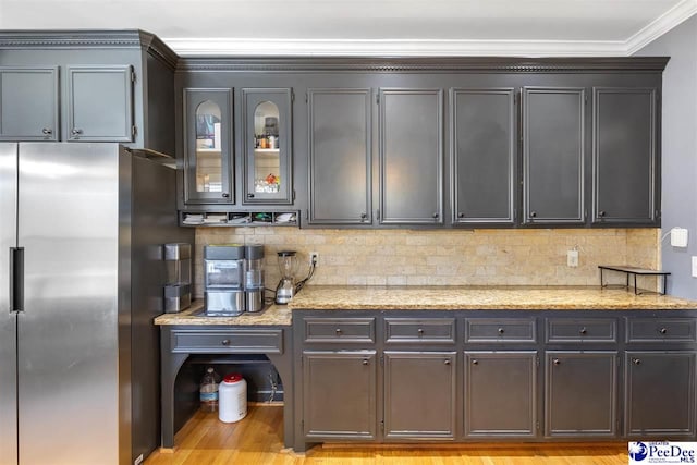 kitchen featuring light stone counters, stainless steel fridge, backsplash, and crown molding