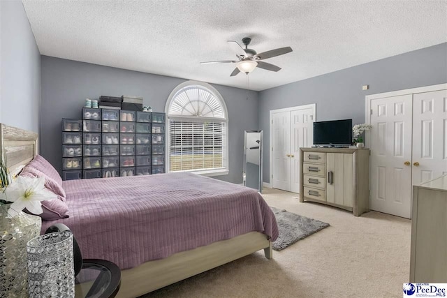 carpeted bedroom featuring a textured ceiling, two closets, and ceiling fan