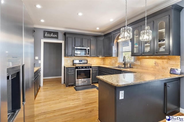 kitchen featuring a peninsula, a sink, ornamental molding, stainless steel appliances, and light wood-style floors