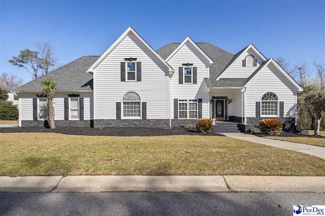 traditional home with stone siding, roof with shingles, and a front yard