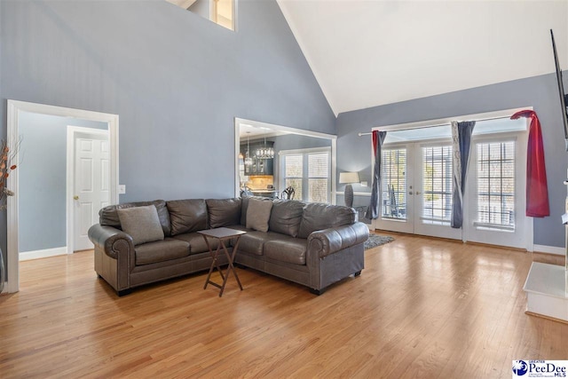 living room with an inviting chandelier, baseboards, light wood finished floors, and high vaulted ceiling