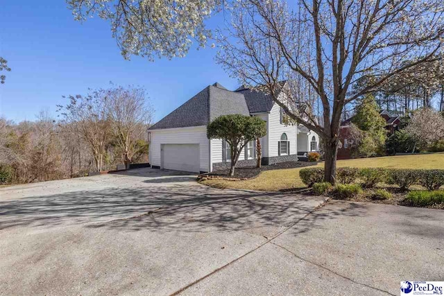 view of side of property with a lawn, driveway, stone siding, roof with shingles, and an attached garage