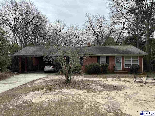 ranch-style house with a carport, brick siding, a chimney, and dirt driveway