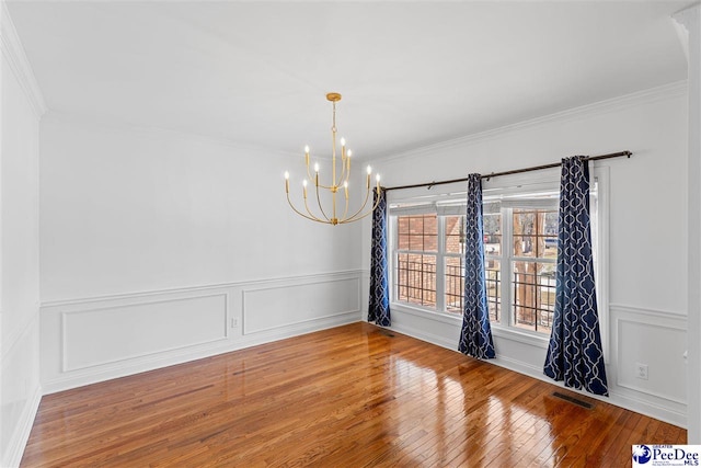 empty room featuring a notable chandelier, a decorative wall, wood-type flooring, and crown molding