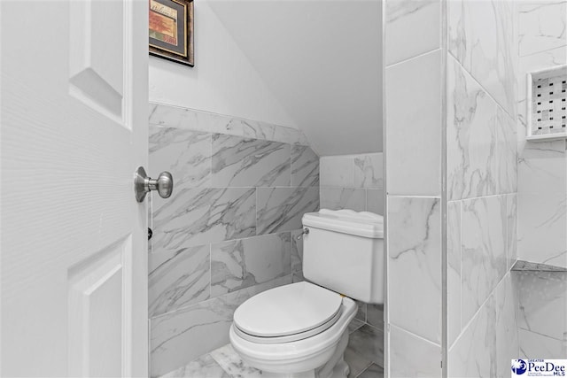 bathroom featuring vaulted ceiling, marble finish floor, toilet, and tile walls