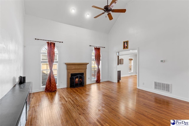 unfurnished living room with plenty of natural light, a lit fireplace, wood-type flooring, and visible vents