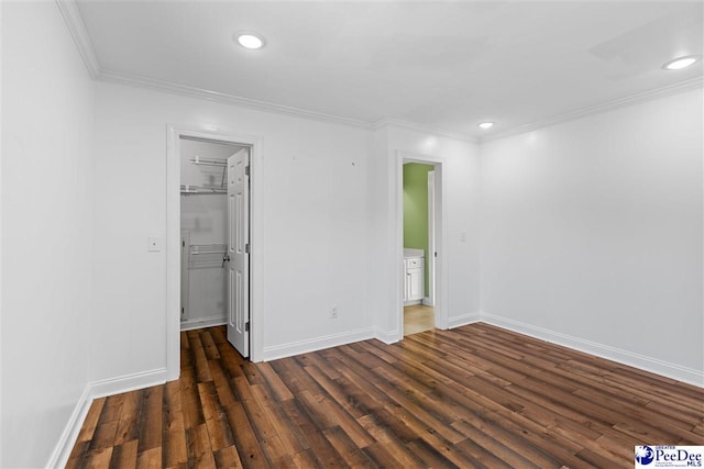 unfurnished bedroom featuring dark wood-style flooring, crown molding, a spacious closet, and baseboards