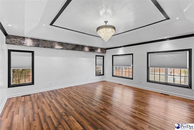 spare room featuring baseboards, wood finished floors, a raised ceiling, and a notable chandelier