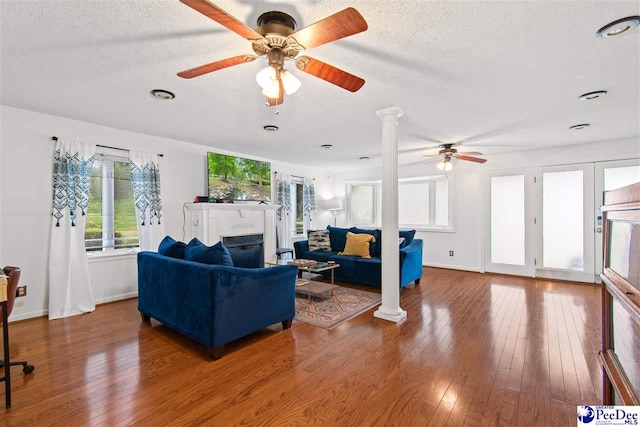 living room with ceiling fan, hardwood / wood-style floors, a textured ceiling, and ornate columns