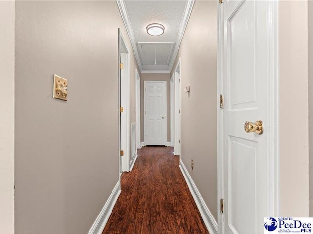 hallway with dark wood-type flooring, attic access, baseboards, a textured ceiling, and crown molding