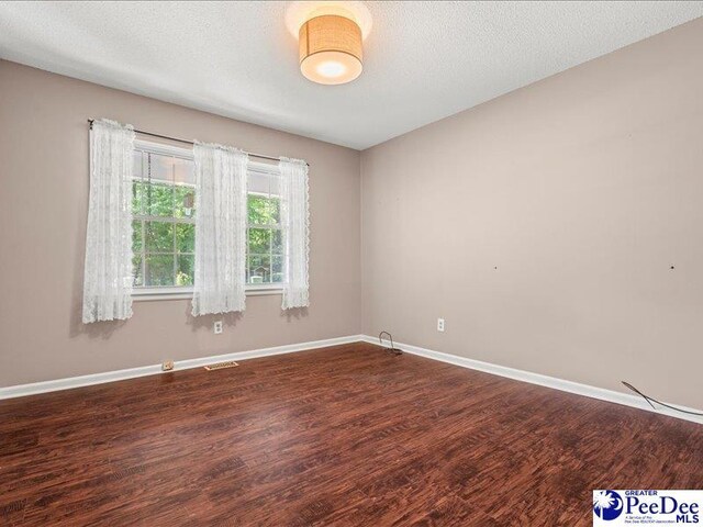 empty room featuring visible vents, dark wood-style floors, and baseboards