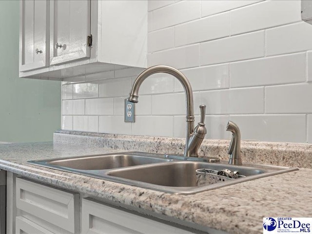 room details with a sink, white cabinets, backsplash, and light countertops