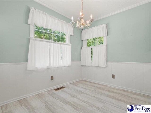 empty room with a chandelier, crown molding, visible vents, and wainscoting