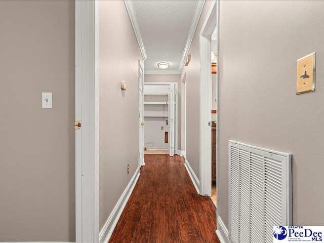 corridor with wood finished floors, visible vents, ornamental molding, and baseboards