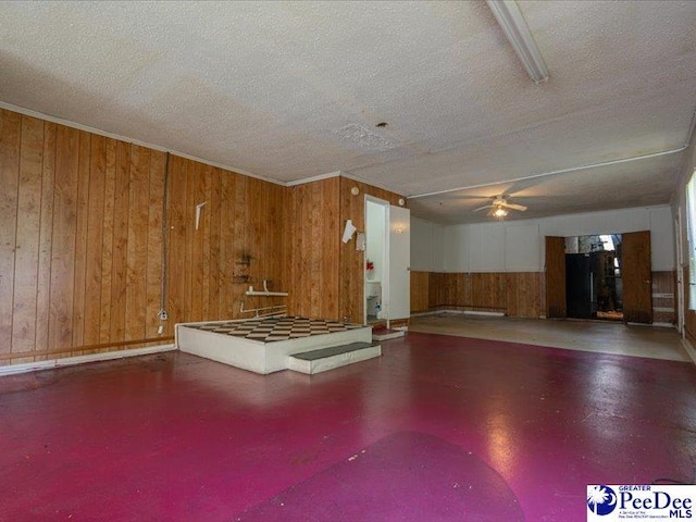 misc room with concrete flooring, ceiling fan, wooden walls, and a textured ceiling