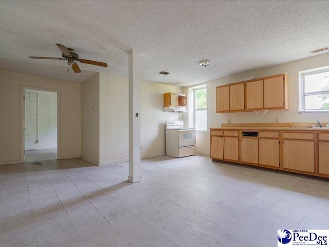 kitchen with white electric stove, light brown cabinets, and a textured ceiling