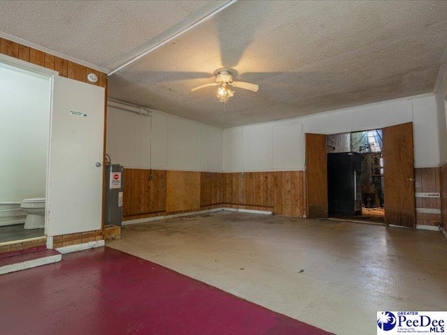 garage with electric water heater, black refrigerator, ceiling fan, and wood walls