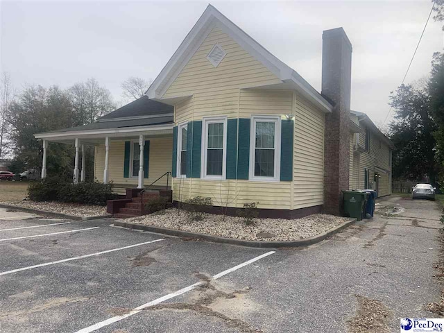 view of front of home with uncovered parking, covered porch, and a chimney