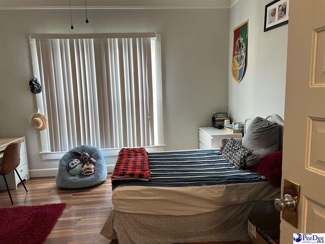 bedroom featuring baseboards, multiple windows, ornamental molding, and wood finished floors