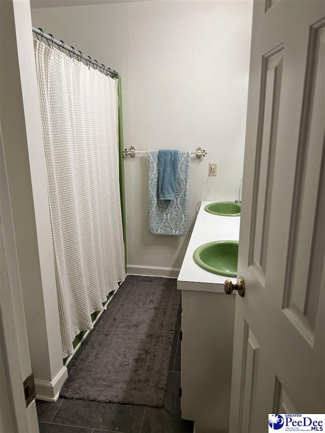 bathroom with double vanity, curtained shower, a sink, tile patterned flooring, and baseboards