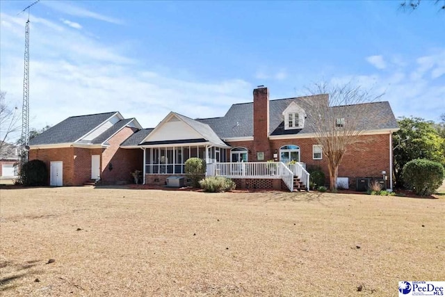 back of property with brick siding, a chimney, a deck, and a sunroom