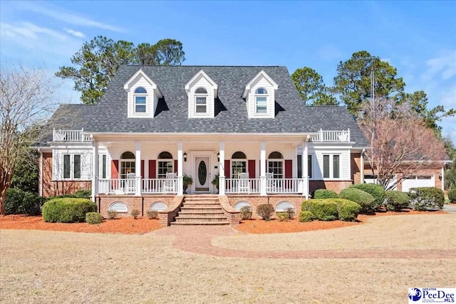 cape cod home featuring a balcony, stairway, covered porch, roof with shingles, and brick siding