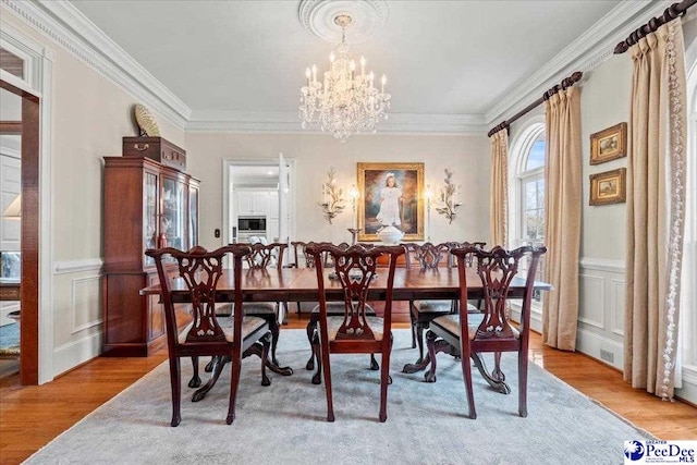 dining area with a wainscoted wall, light wood-type flooring, a chandelier, and ornamental molding