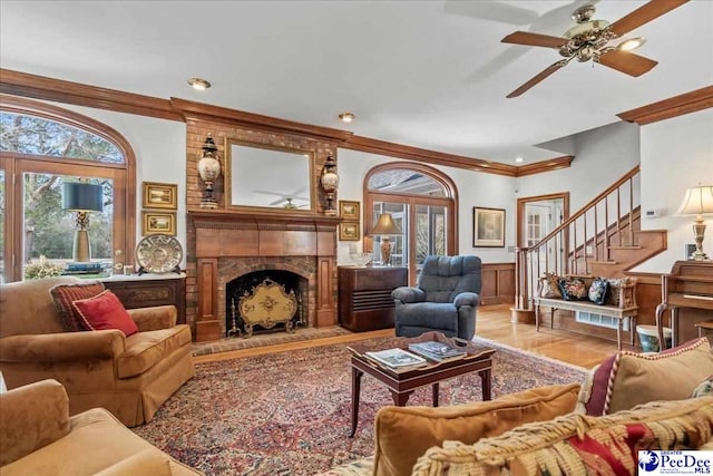 living area featuring a wainscoted wall, a fireplace, wood finished floors, and ornamental molding