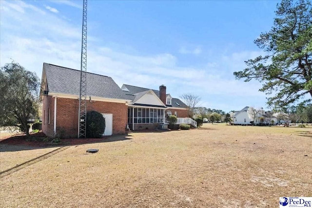 rear view of property featuring brick siding, a sunroom, and a chimney