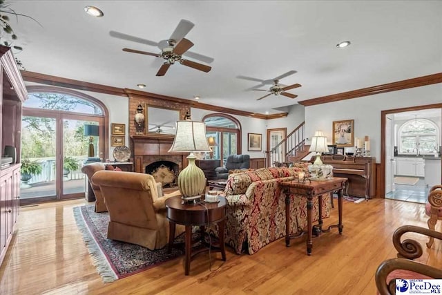 living room featuring crown molding, stairway, light wood-type flooring, and a large fireplace