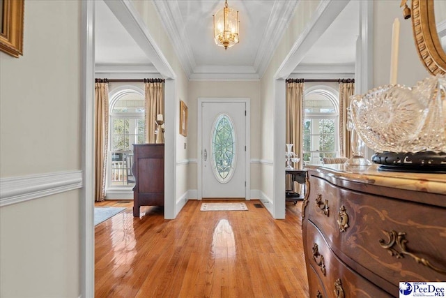 entryway with an inviting chandelier, a healthy amount of sunlight, light wood-style floors, and ornamental molding