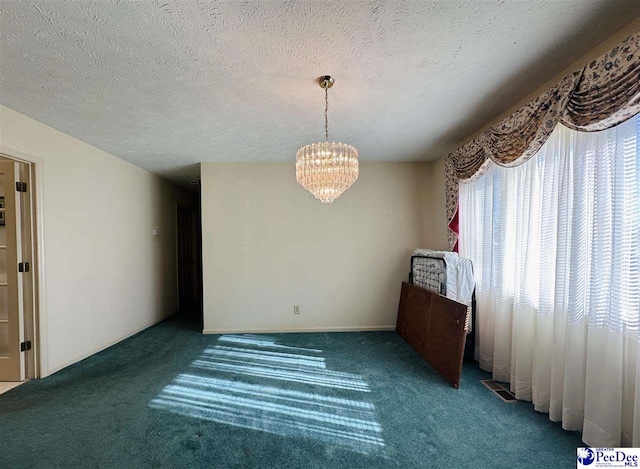 empty room featuring dark carpet, a textured ceiling, and a chandelier