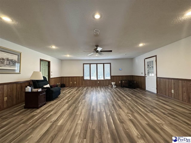 living room with dark hardwood / wood-style flooring, wooden walls, ceiling fan, and a textured ceiling