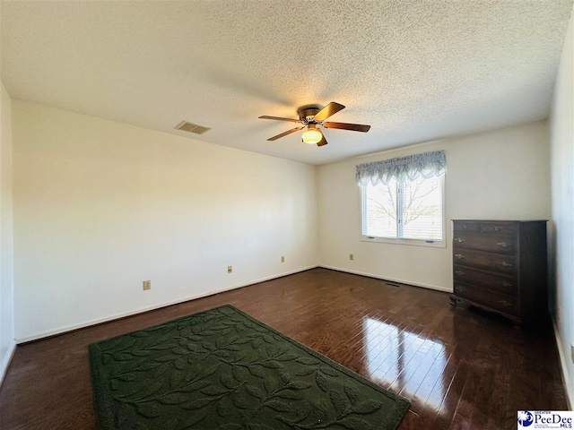 empty room featuring ceiling fan, dark wood-type flooring, and a textured ceiling