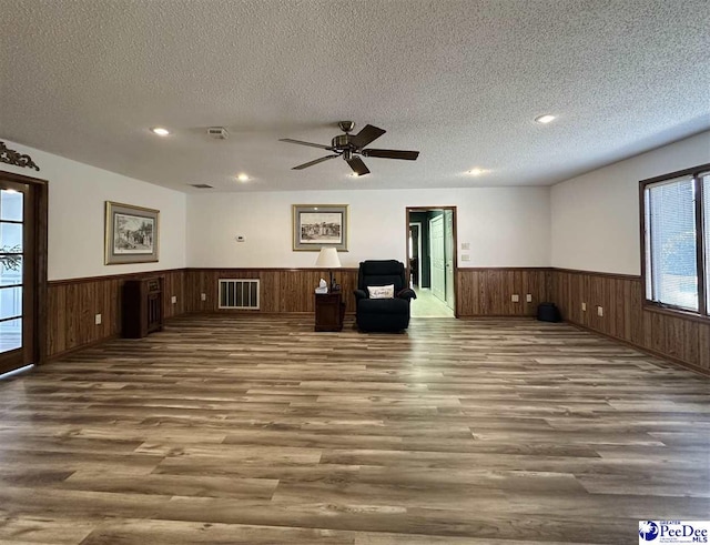 interior space with ceiling fan, hardwood / wood-style floors, a textured ceiling, and wood walls