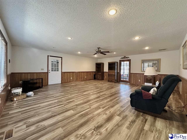 living room featuring ceiling fan, a textured ceiling, light wood-type flooring, and wood walls