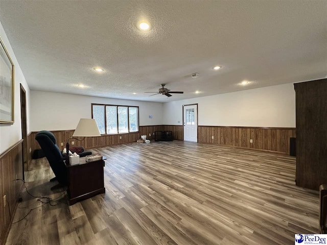 living room with hardwood / wood-style flooring, ceiling fan, a textured ceiling, and wood walls