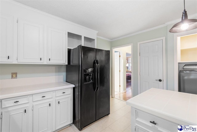 kitchen with tile countertops, washer / dryer, white cabinets, hanging light fixtures, and black fridge