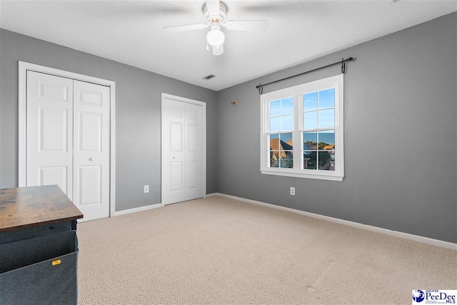 unfurnished bedroom featuring ceiling fan, a textured ceiling, multiple closets, and carpet