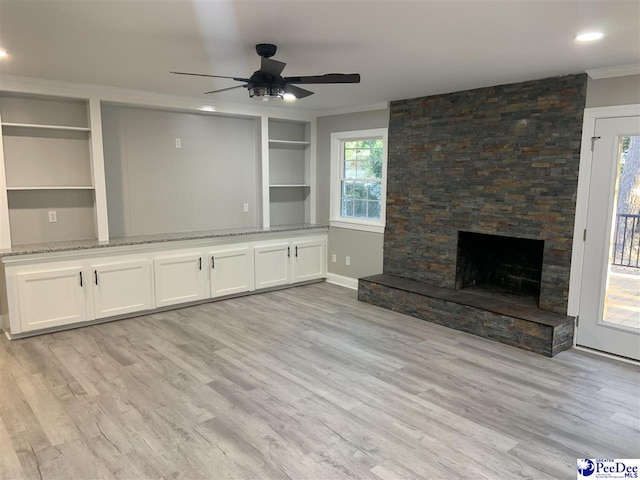 unfurnished living room featuring crown molding, ceiling fan, a fireplace, built in shelves, and light wood-type flooring