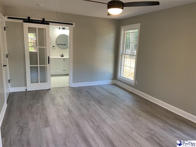 empty room featuring ceiling fan, light hardwood / wood-style flooring, a barn door, and a healthy amount of sunlight