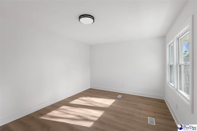 empty room featuring visible vents, baseboards, and wood finished floors
