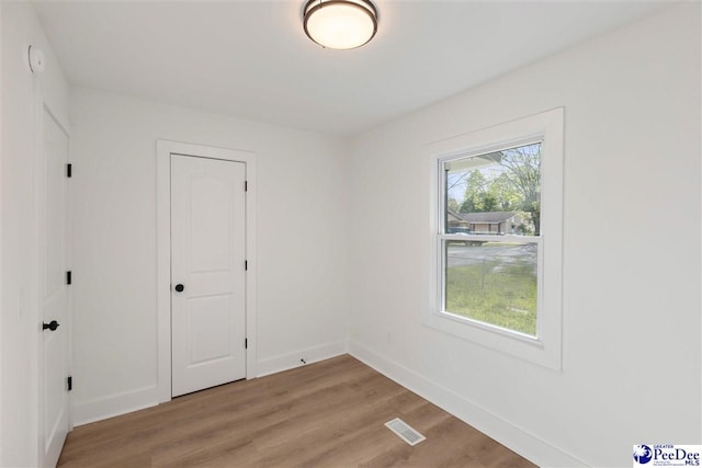 empty room featuring light wood finished floors, baseboards, and visible vents