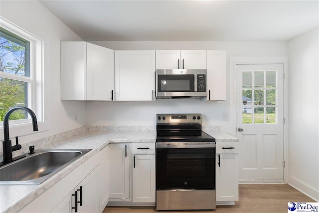kitchen with a sink, light wood-style flooring, appliances with stainless steel finishes, and white cabinetry