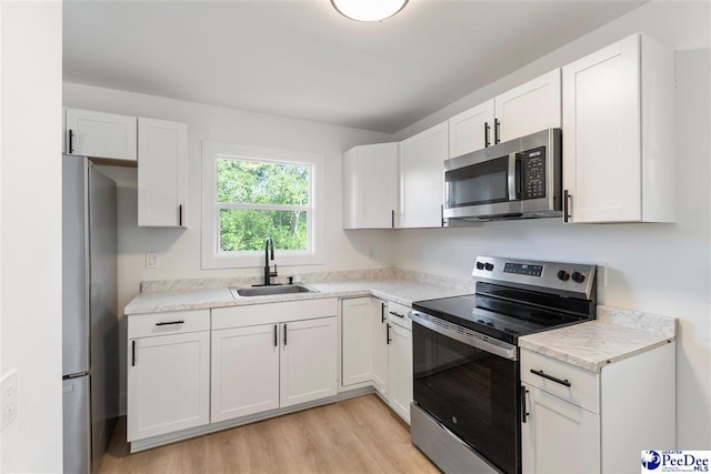 kitchen featuring light wood-style flooring, white cabinets, appliances with stainless steel finishes, light countertops, and a sink