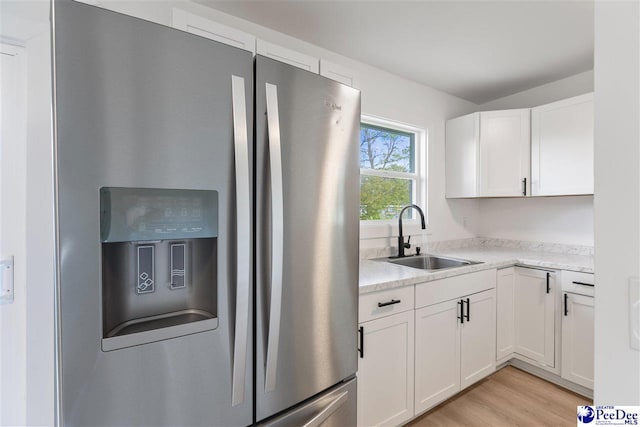 kitchen with light wood-type flooring, white cabinets, light stone counters, a sink, and stainless steel fridge